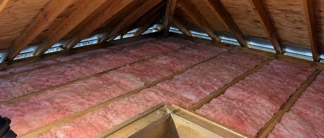 Pink fiberglass batts laid around a framed attic hatch opening in a finished attic floor