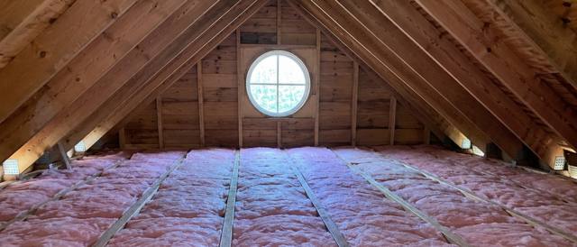 Pink batts between joists across a whole attic, with a round window in the gable wall