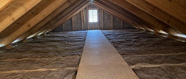 Tan fiberglass batts between attic joists on each side of a plywood walkway leading to a gable vent
