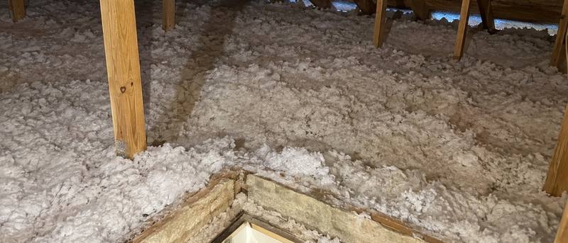White loose-fill insulation filling an attic around a framed hatch opening in the floor